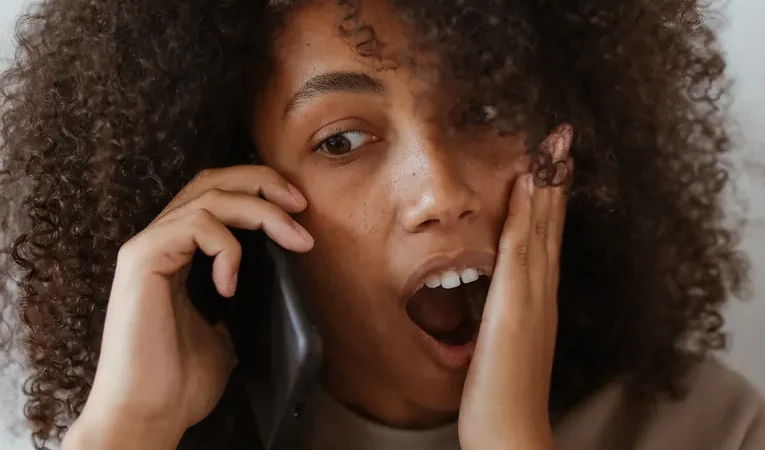 Woman appearing shocked while talking on the phone, illustrating AI voice cloning scam calls
