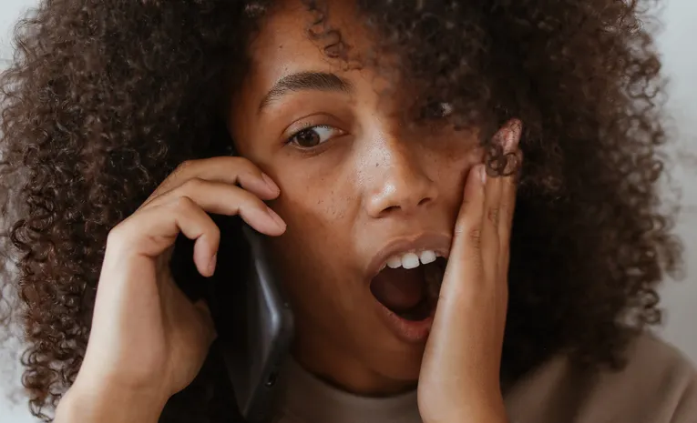 Woman appearing shocked while talking on the phone, illustrating AI voice cloning scam calls