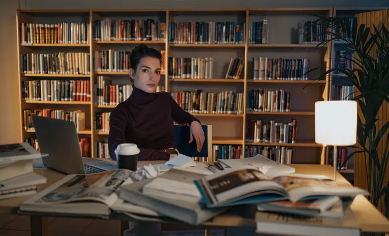 Researcher working with books and a laptop in a library, illustrating the Elicit AI research assistant review
