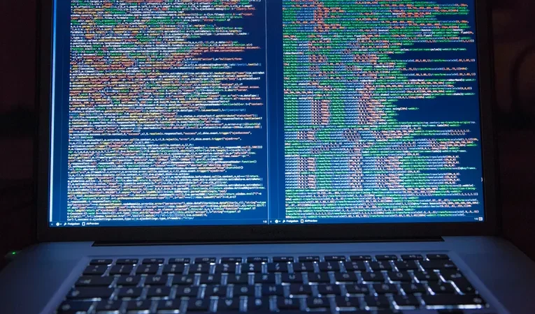 Developer coding on a laptop with a dual monitor setup, illustrating the Emergent AI app builder review