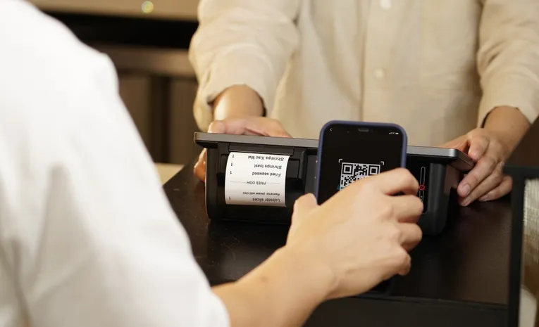 Close-up of a person scanning a QR code with a smartphone at a retail counter